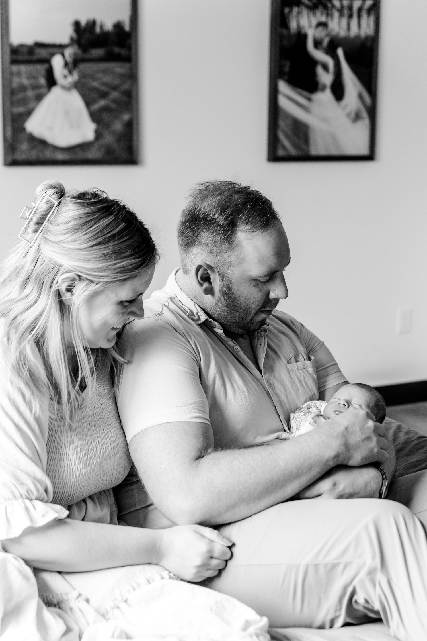 Black and white photo of new parents gazing lovingly at their newborn baby at home.