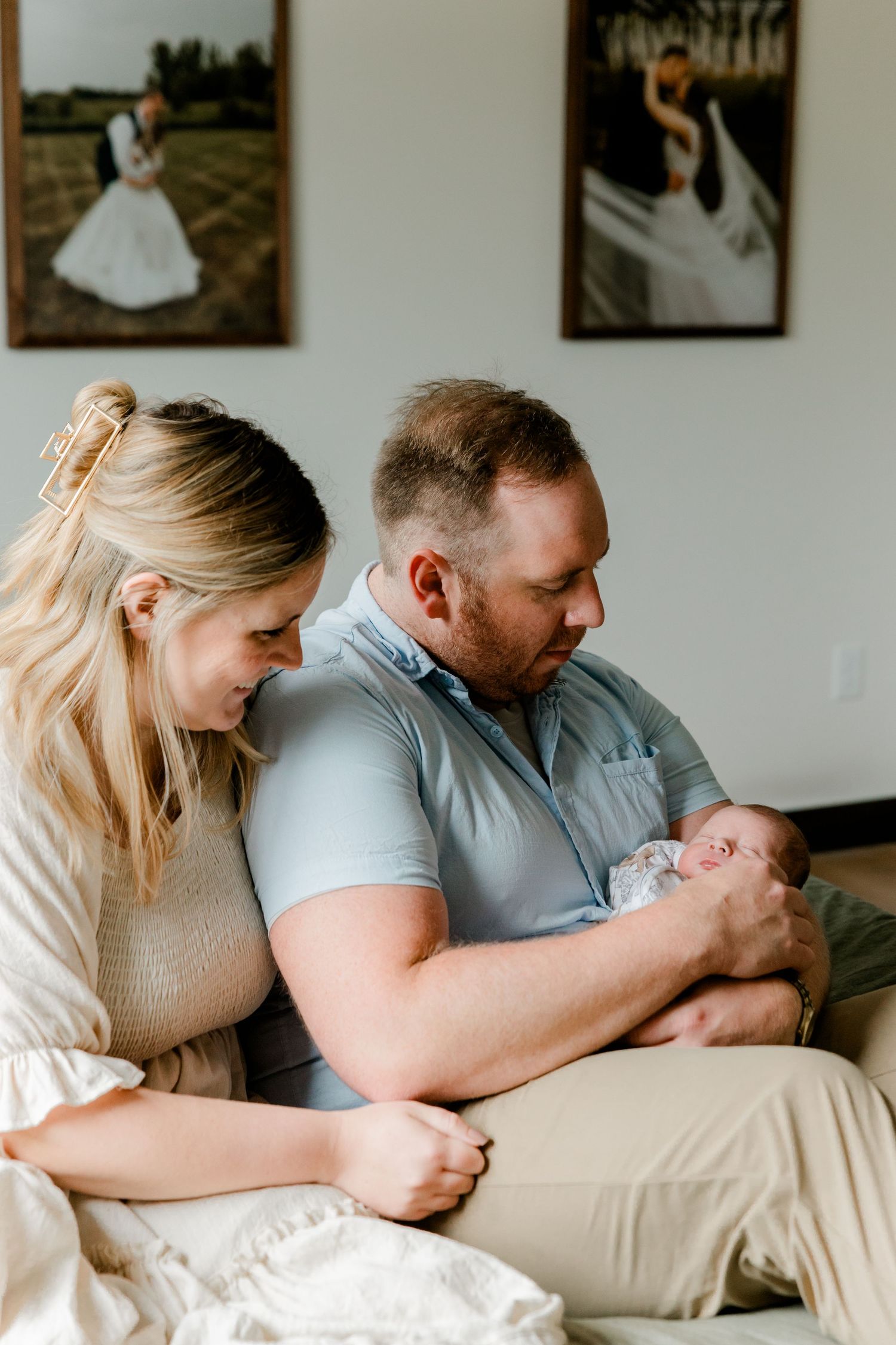 New parents lovingly gaze at their newborn baby while sitting together on a couch at home.