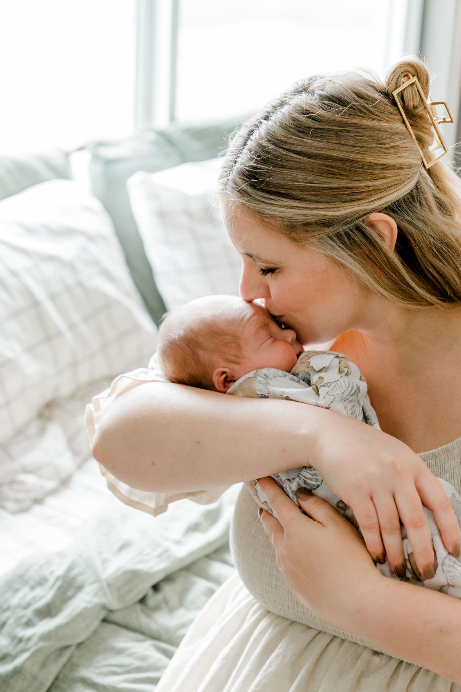 A new mother tenderly kisses her sleeping newborn baby while cradling them gently in her arms.