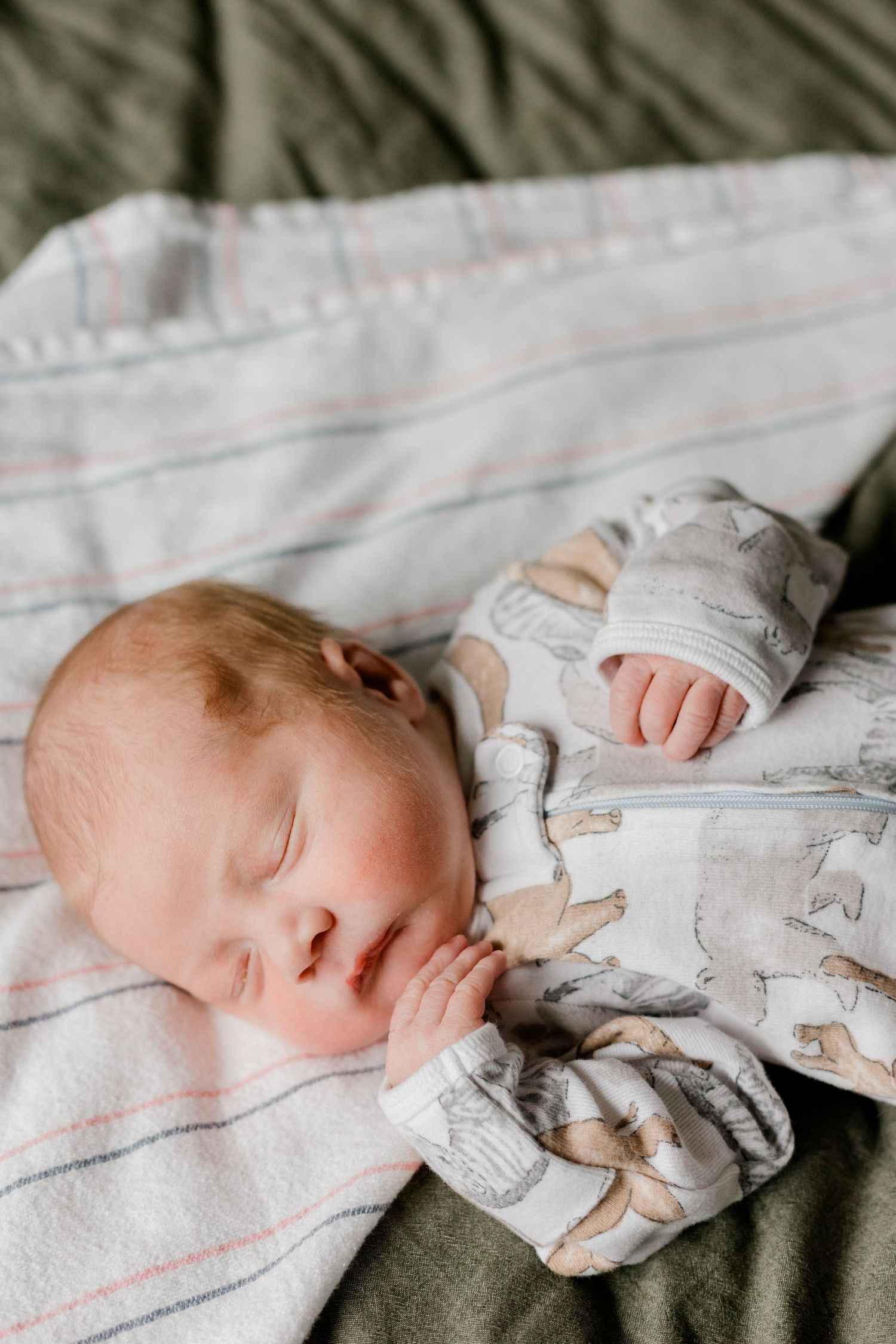 A peaceful newborn baby sleeps soundly in a animal-print onesie on a striped blanket.