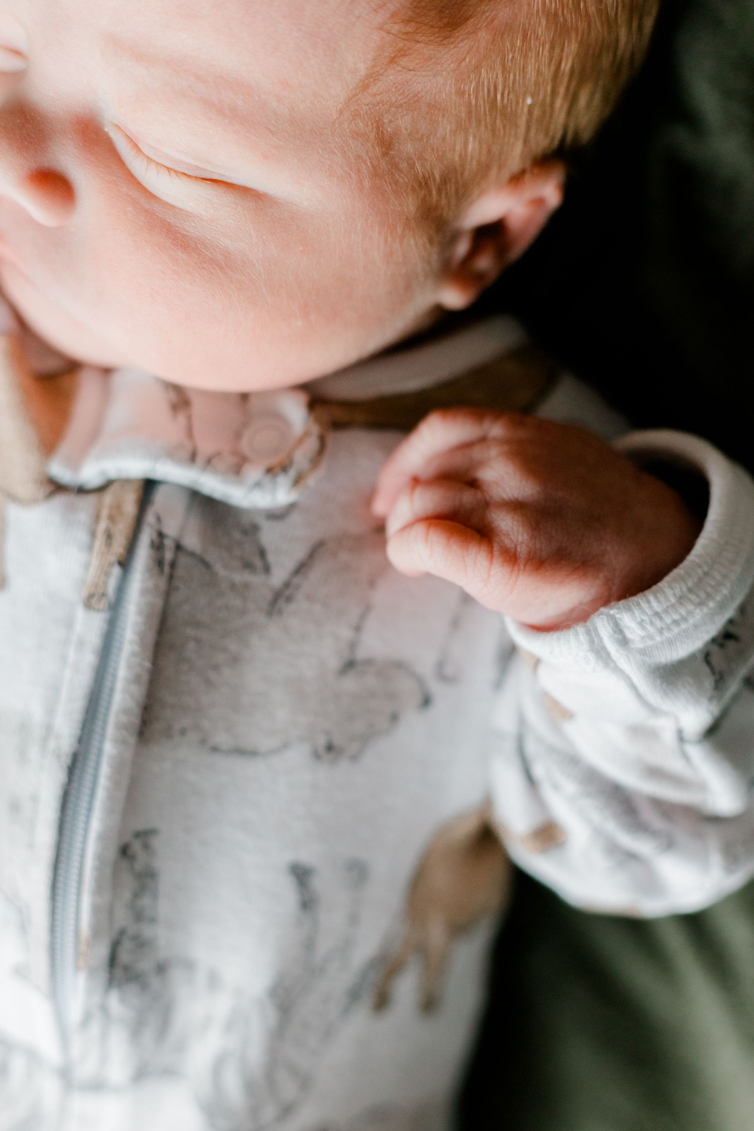 Close-up of a newborn baby's tiny clenched fist resting on an animal-print onesie.