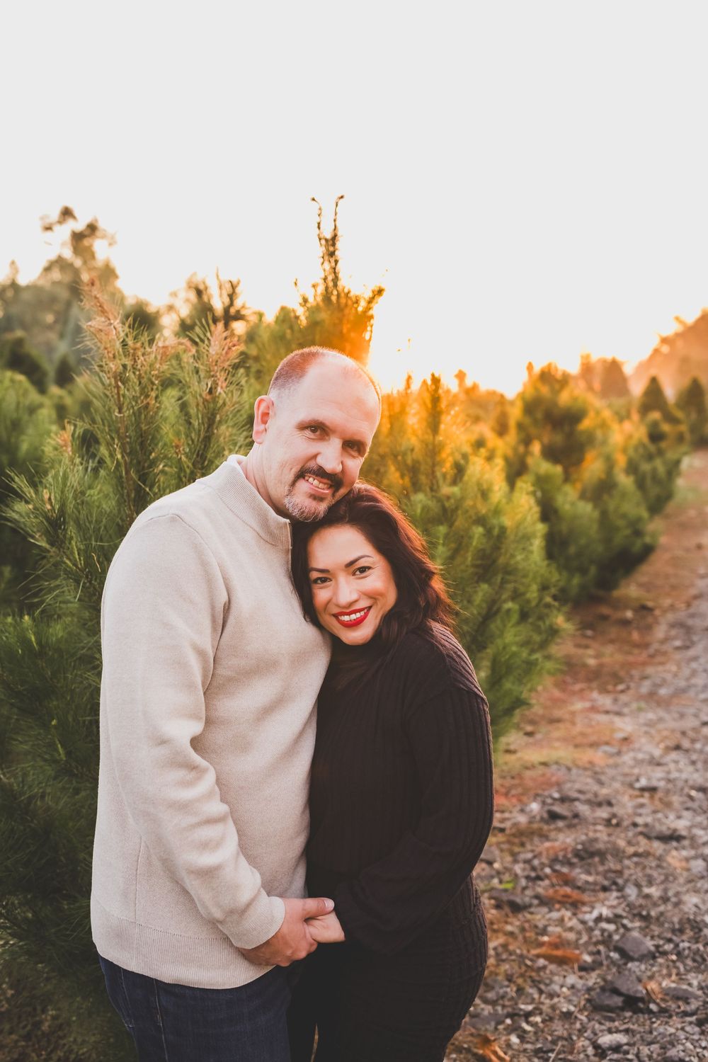 A couple shares a joyful moment together among evergreen trees during golden hour sunset.