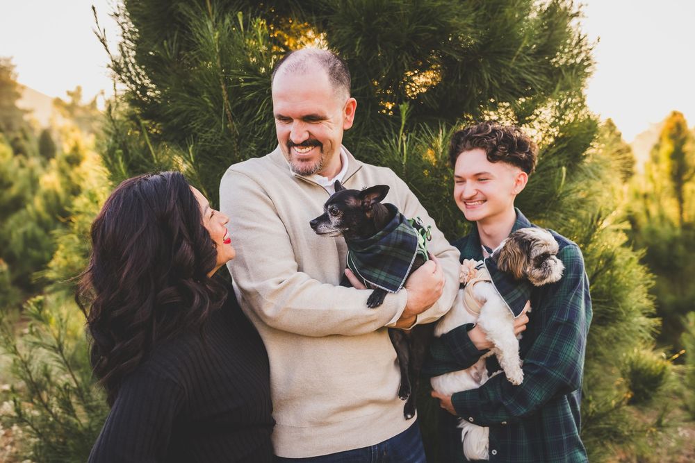 Family and pets gather for casual portraits by evergreen trees during sunset photography session.