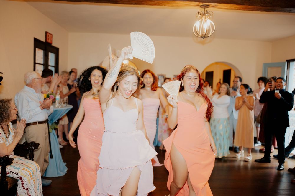 Wedding guests dancing and celebrating at a reception with people wearing colorful formal dresses in pink and blue tones.
