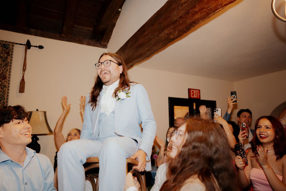 Wedding guests dancing and celebrating in a reception hall with exposed wooden beams.