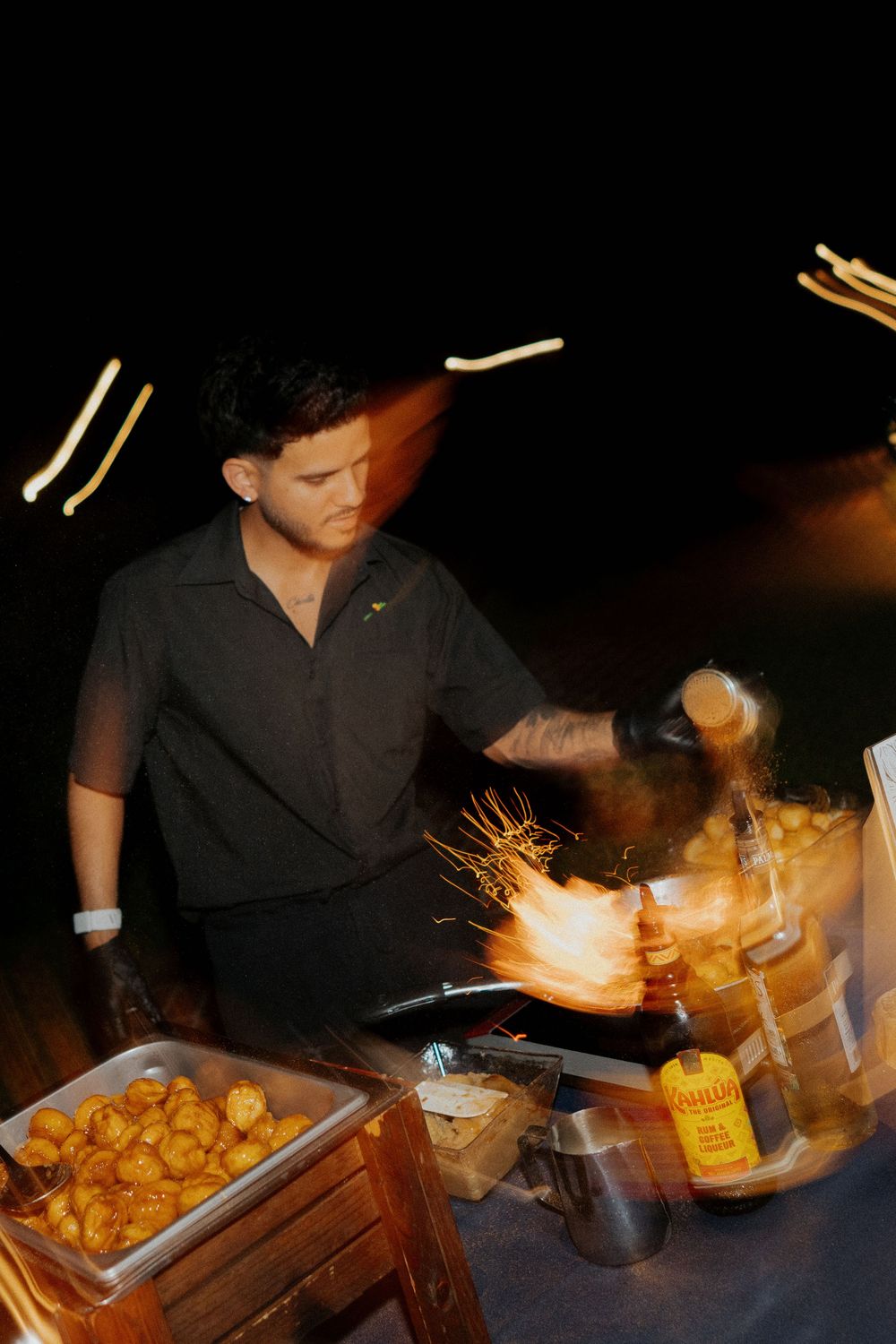 Chef preparing flaming dishes at a dimly lit catering station.