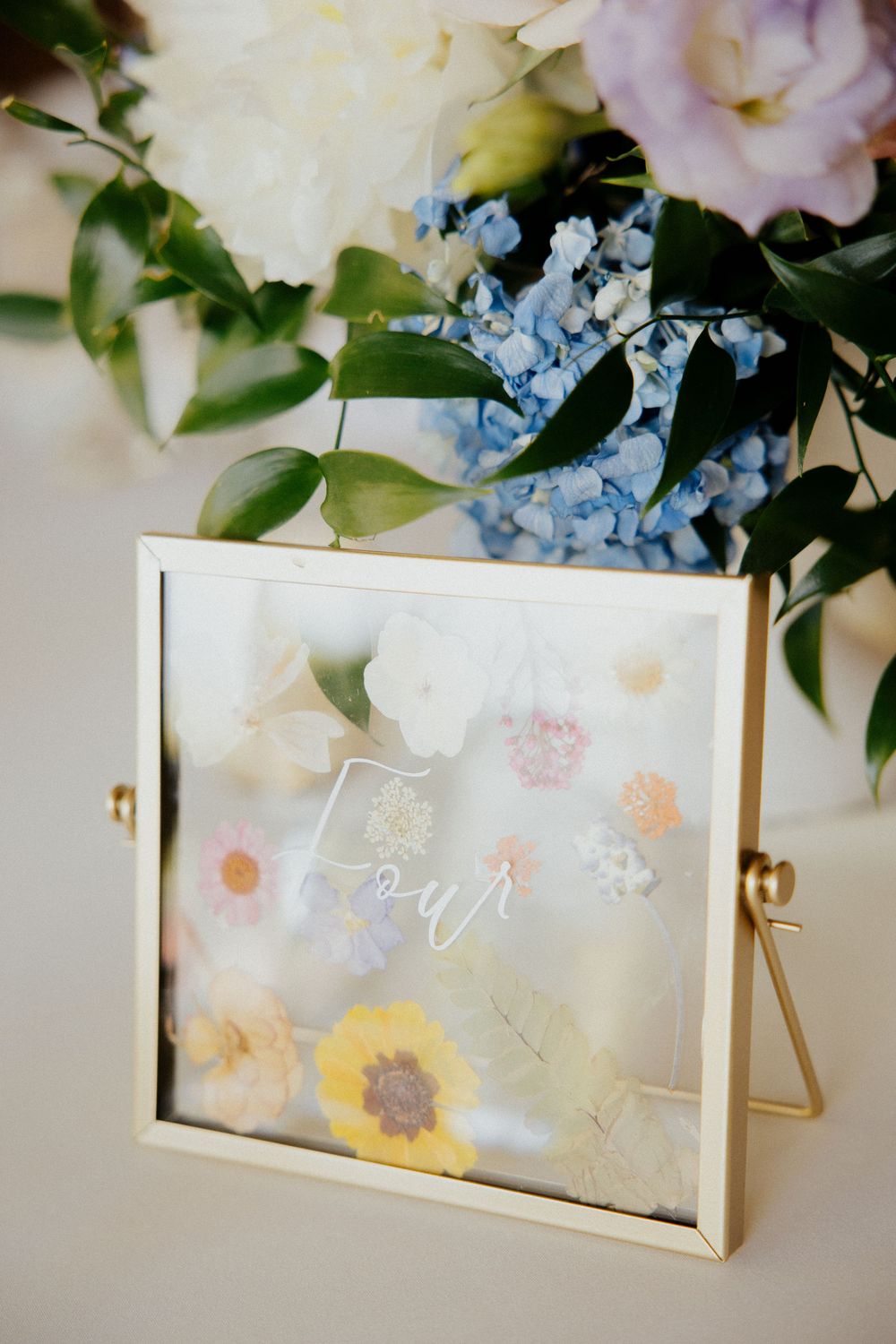Delicate floral table decor with white and blue flowers arranged around transparent acrylic display frames.
