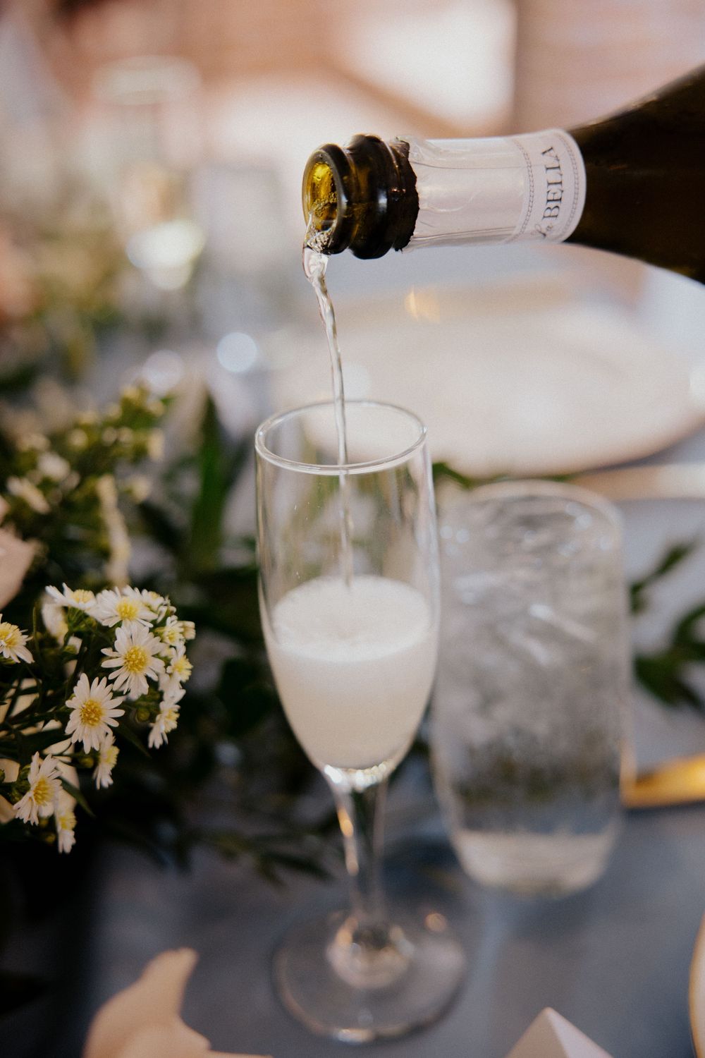 Champagne being poured into glasses with daisy flower decorations on the table.