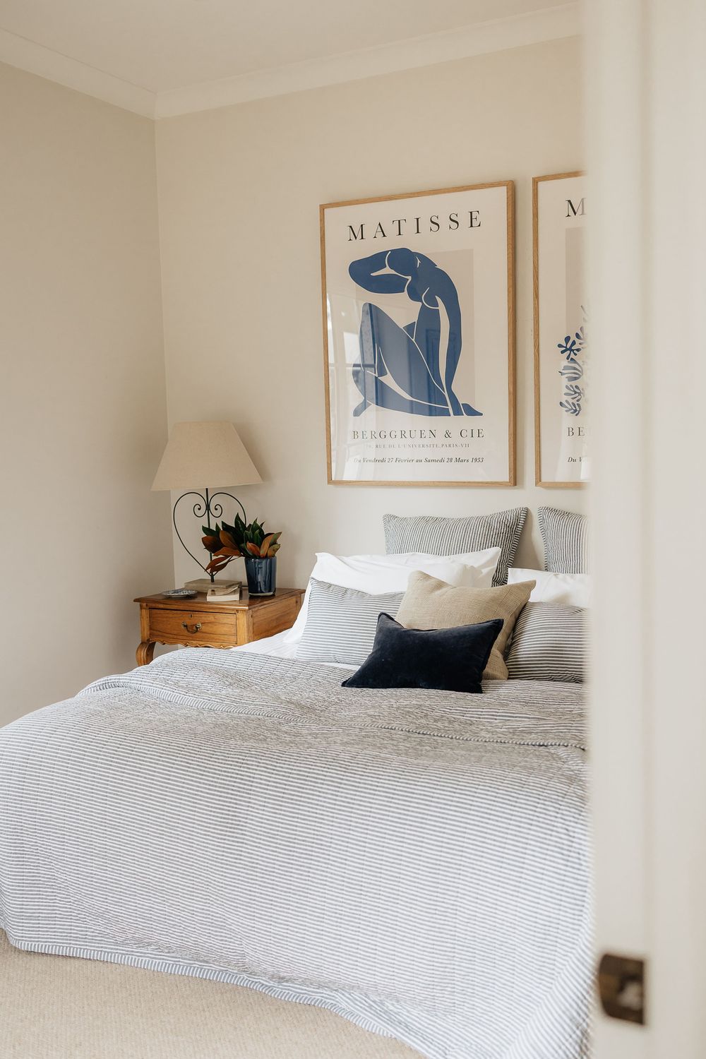 Minimalist bedroom with white bedding, Matisse art prints, and natural wood accents creates a serene atmosphere.