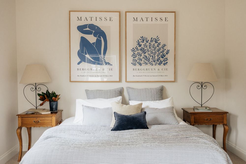 Modern bedroom with Matisse artwork, white bedding, navy accents, and natural light streaming through windows.