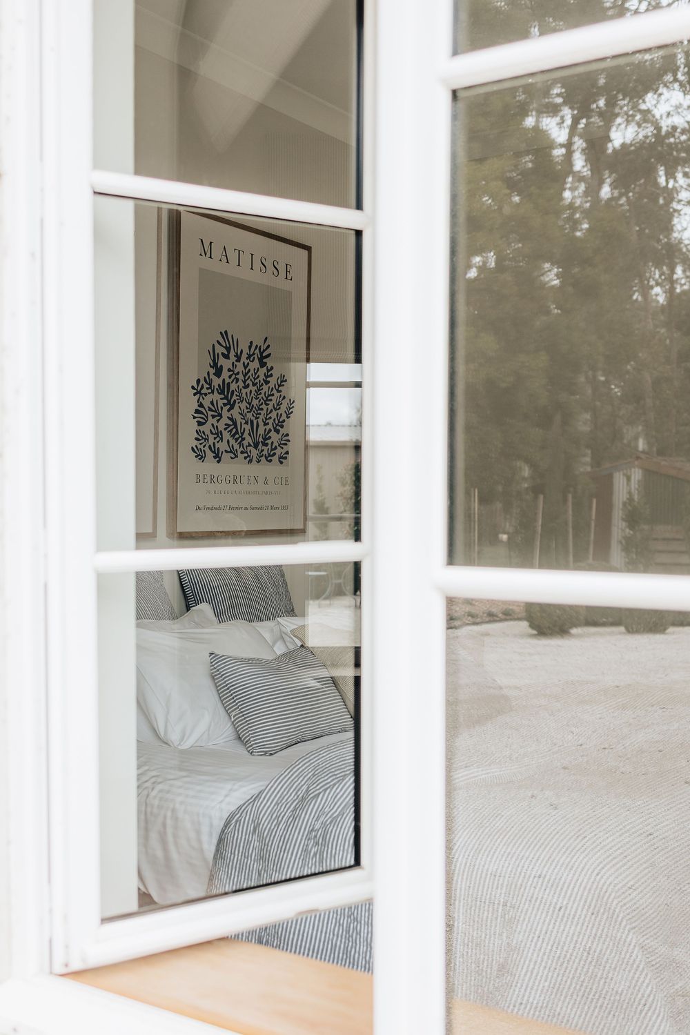 A cozy bedroom window view showing white bedding and a Matisse art print on display.