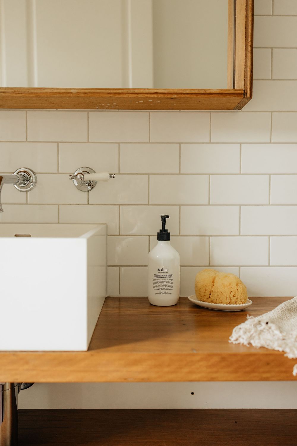 Modern bathroom interior with wooden countertop, white subway tile backsplash, and minimalist decor accessories.