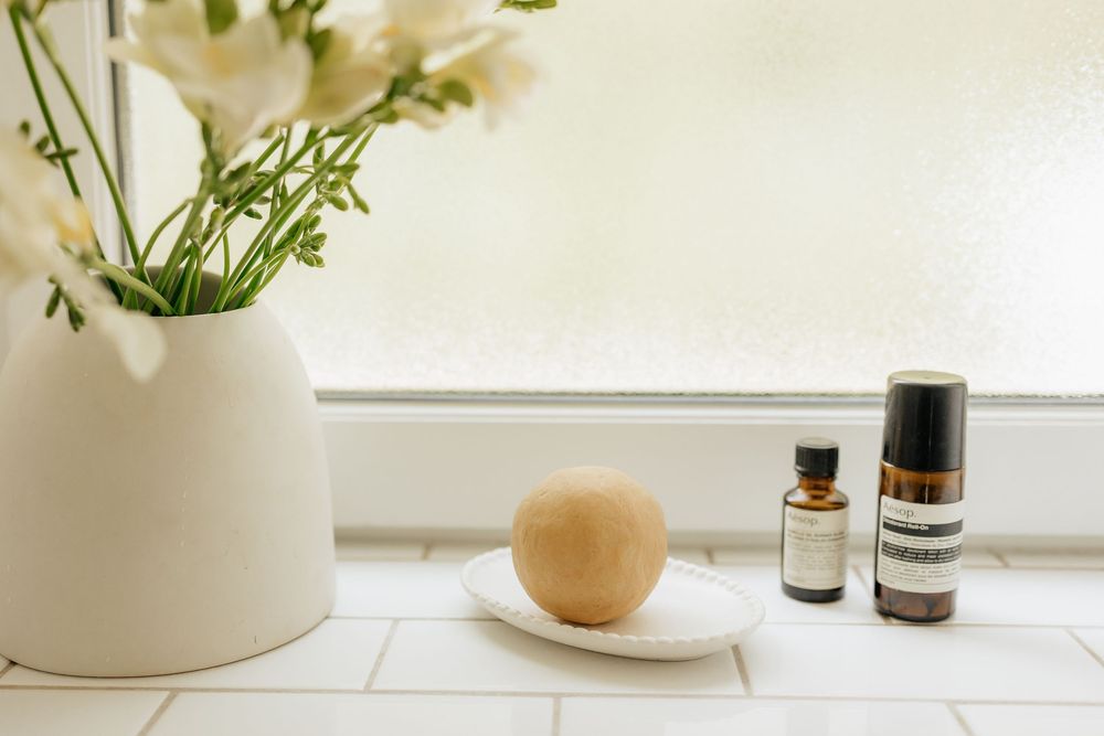 White ceramic vase with fresh flowers sits on windowsill beside essential oil bottles and natural soap bar.