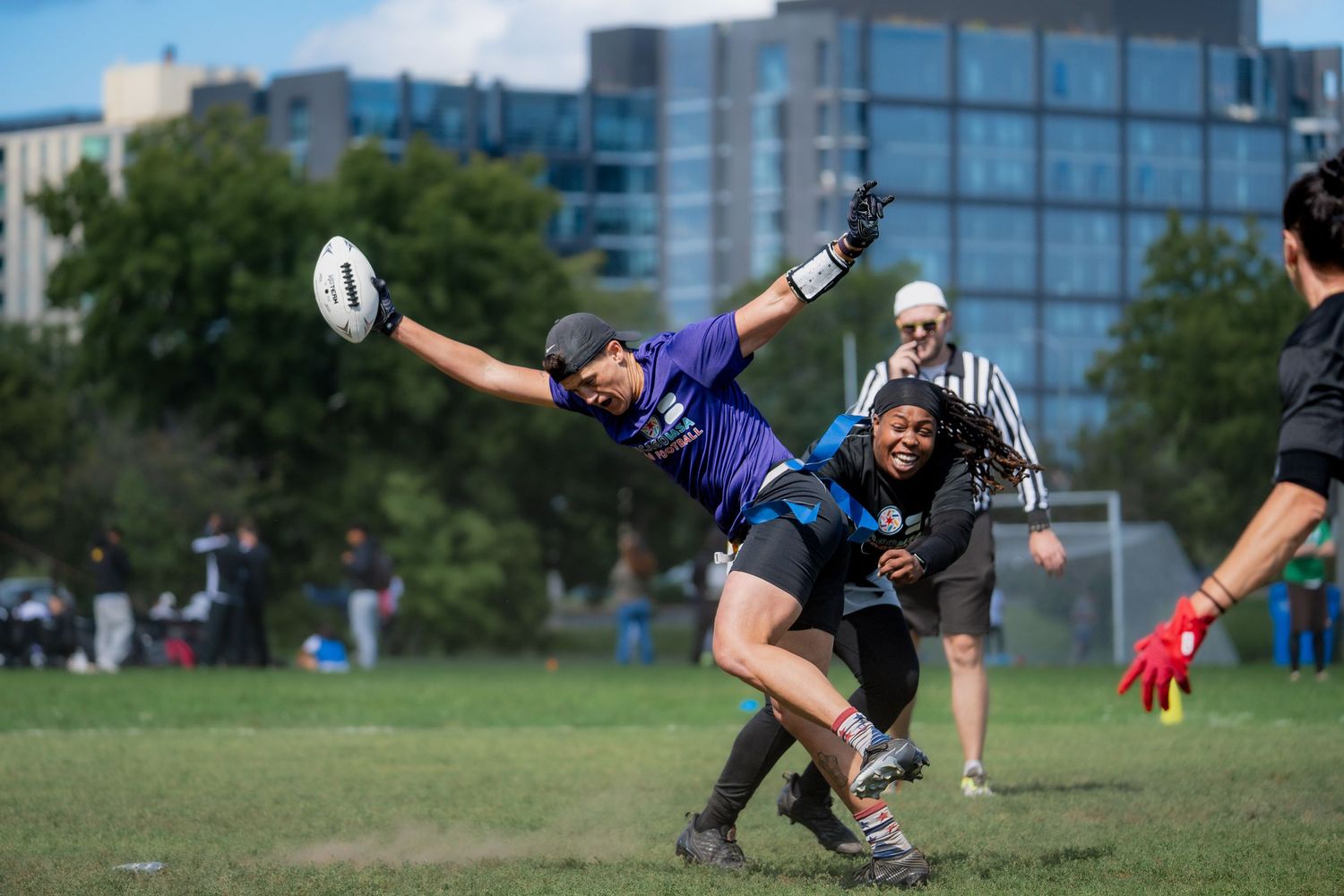 A football athlete attempts to avoid the flag pull from a defensive player behind them, with the football outstretched in their arm