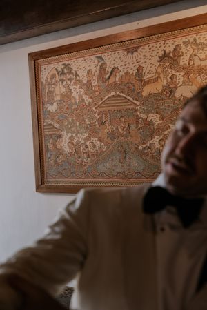 Decorative ornate framed artwork with intricate patterns hangs on a white wall in warm lighting.