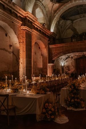 Elegant candlelit banquet tables set inside a historic stone monastery with vaulted ceilings and ornate architectural details.