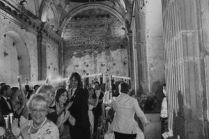 Wedding guests dancing and celebrating inside a historic stone building with arched columns.