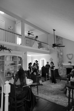 A panoramic view of people gathered in a modern open-concept living room with white walls and built-in shelving.