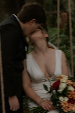 A romantic wedding moment captured in a forest setting with a white dress and vibrant floral bouquet.