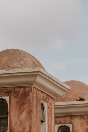 A series of terracotta-colored domed buildings with curved architectural details against a light blue sky.