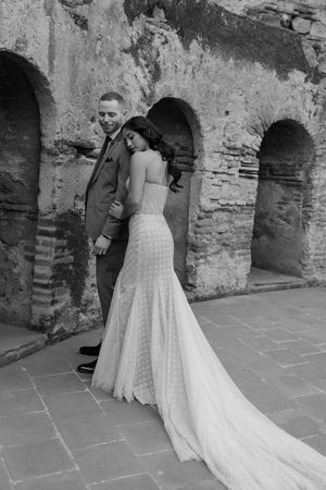 A bride in a white polka dot wedding dress with a flowing train poses against historic stone archways.