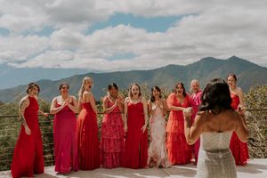 A group in red and pink dresses poses together against a scenic mountain landscape backdrop.