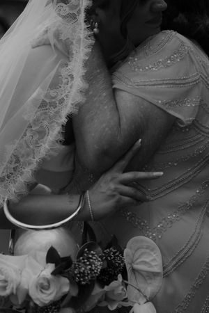A black and white close-up of delicate lace and pearl details on elegant bridal attire.