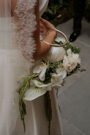 Close-up view of elegant white bridal bouquet featuring roses, anthurium flowers and cascading greenery details.