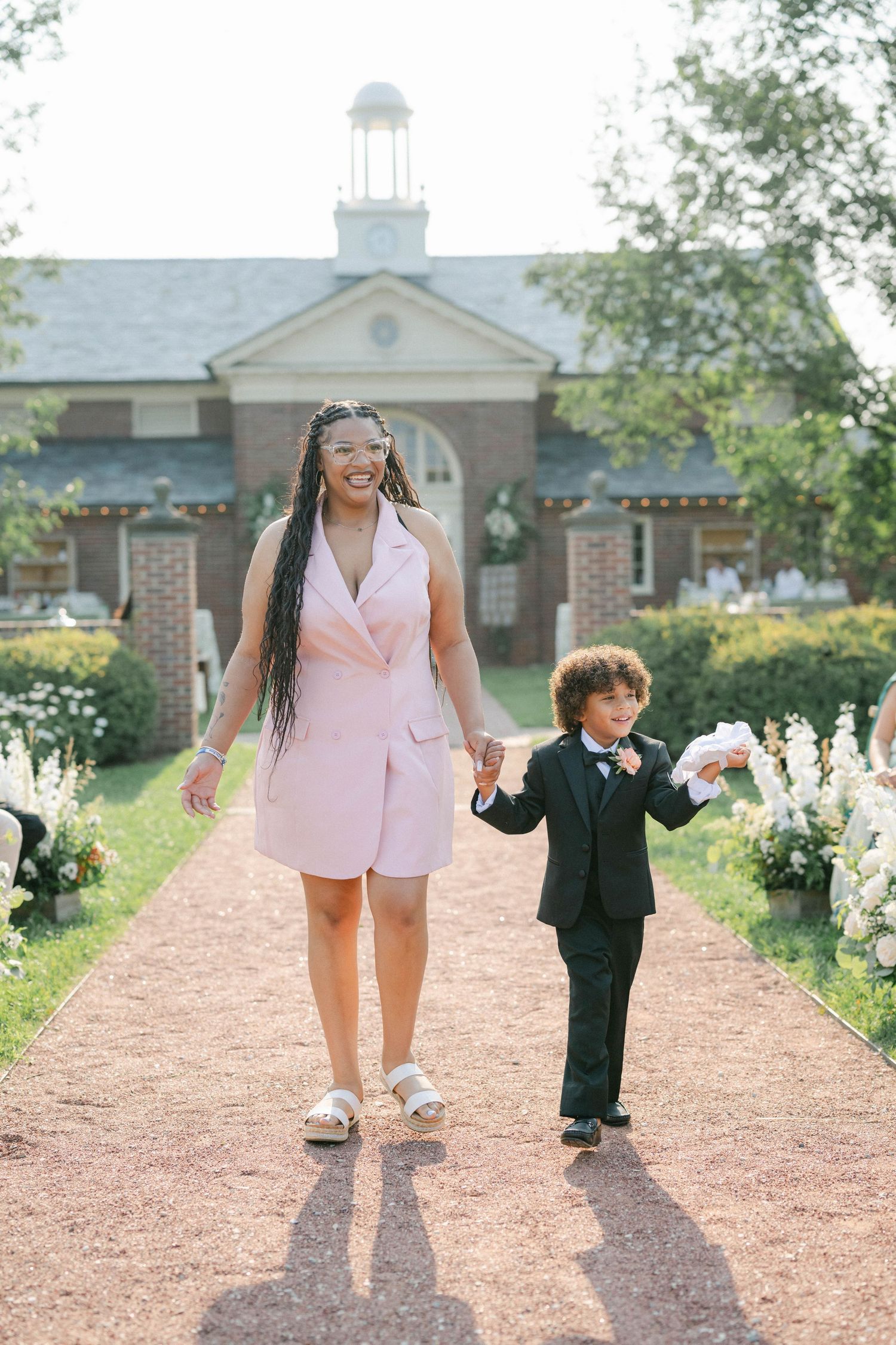 Two people walk together holding hands on a garden path surrounded by greenery and flowers on a sunny day. - Elawa Farm