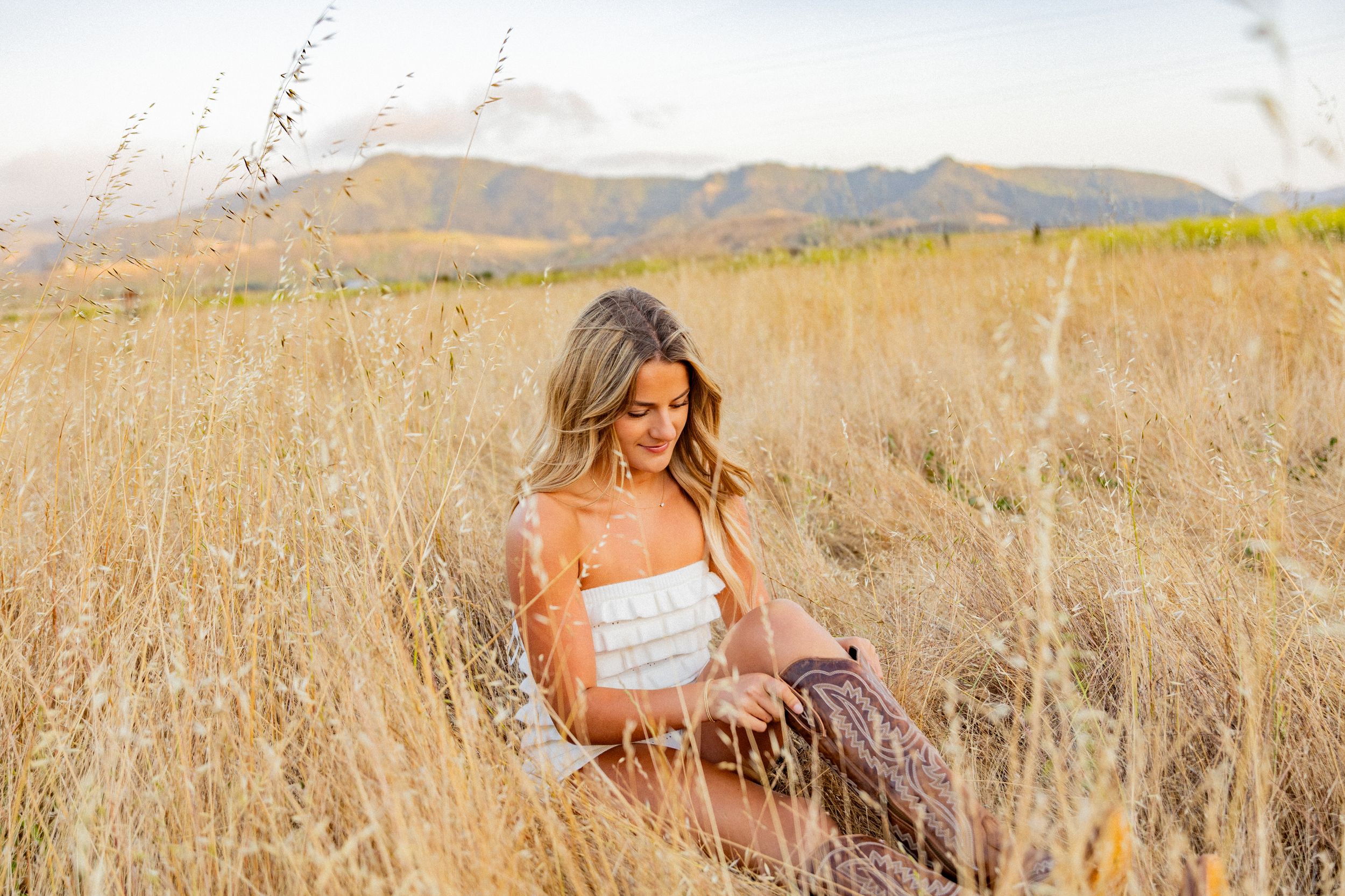 Dreamy golden hour portrait in a rustic field of tall grass with mountains in the background.