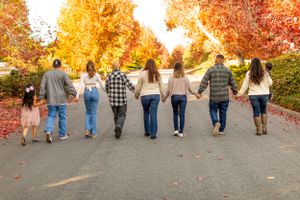 Group of friends walking hand in hand down a path surrounded by vibrant fall foliage.