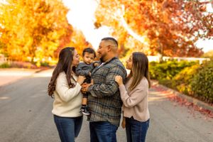 Family embracing and sharing a tender moment on a tree-lined autumn path.