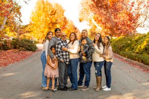 Group family photo with warm autumn colors and falling leaves in background.