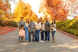 Family portrait on tree-lined path with bright fall foliage overhead.