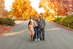 Family group standing close together on a pathway with autumn trees glowing golden behind them.