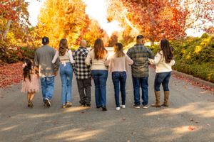 Back view of family walking together on path surrounded by vibrant autumn trees.
