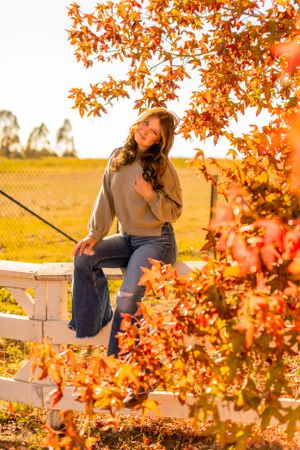 Casual autumn portrait on white fence with golden light and fall foliage.