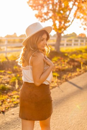 Side profile portrait in warm sunlight showing western-inspired outfit with hat and suede skirt.