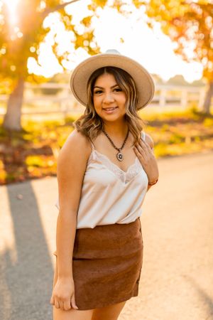 A stylish fall outfit featuring a white camisole, brown suede skirt and wide brim hat captured at golden hour.