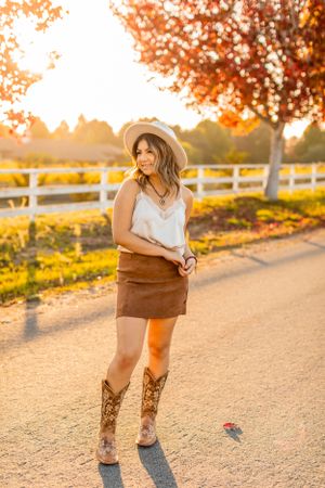 Western-inspired autumn outfit photographed on dirt path with fall foliage and white fence backdrop.