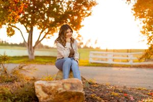 Casual portrait on stone seating with blue jeans and white top against autumn scenery.