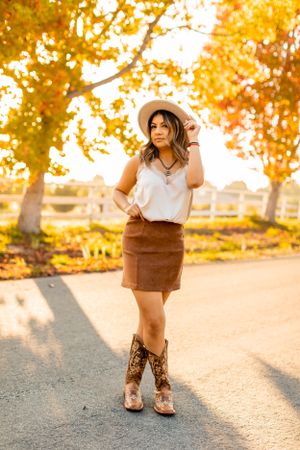 Autumn fashion look featuring cowboy boots, suede skirt and white top against golden foliage.