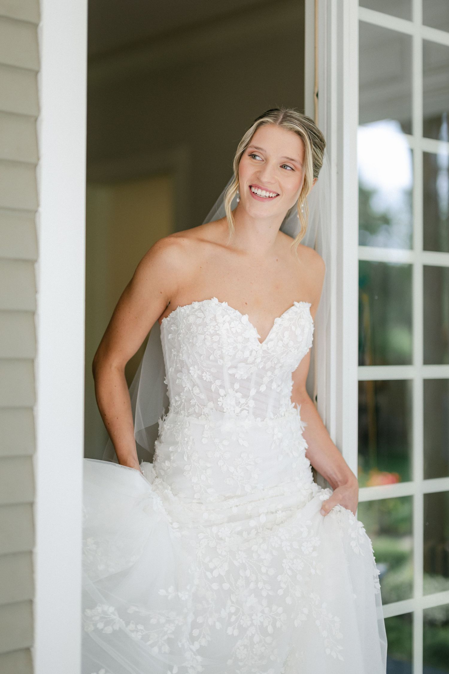 A stunning white wedding gown with intricate lace details and sweetheart neckline is showcased in a doorway setting. - Lake Forest