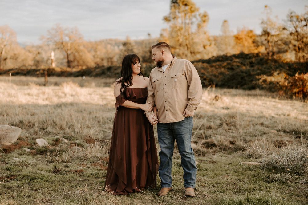 Couple embraces in golden sunlight on a grassy hillside during autumn sunset.
