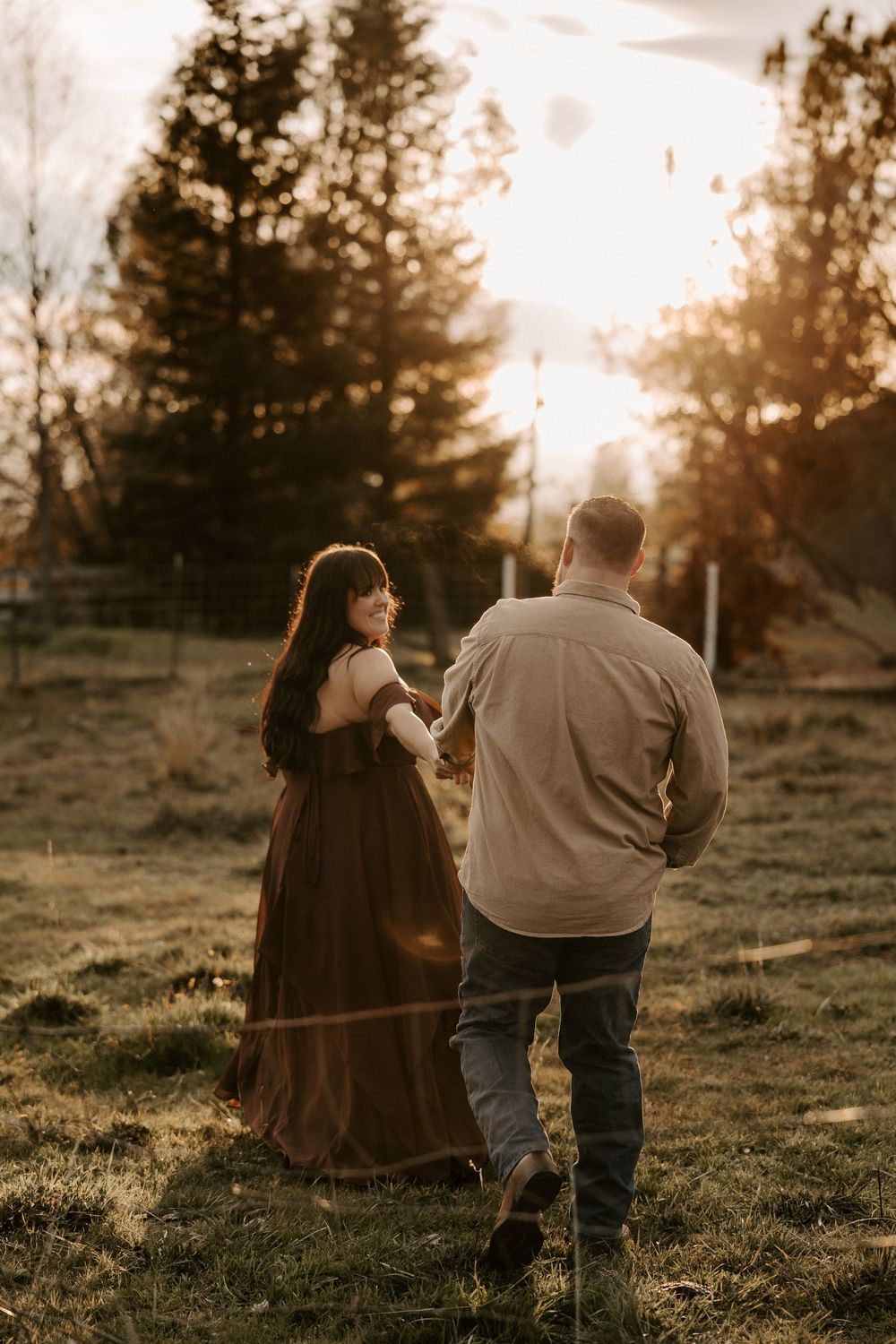 A romantic couple walks together on a hillside during golden hour sunset creating silhouettes against the warm sky.