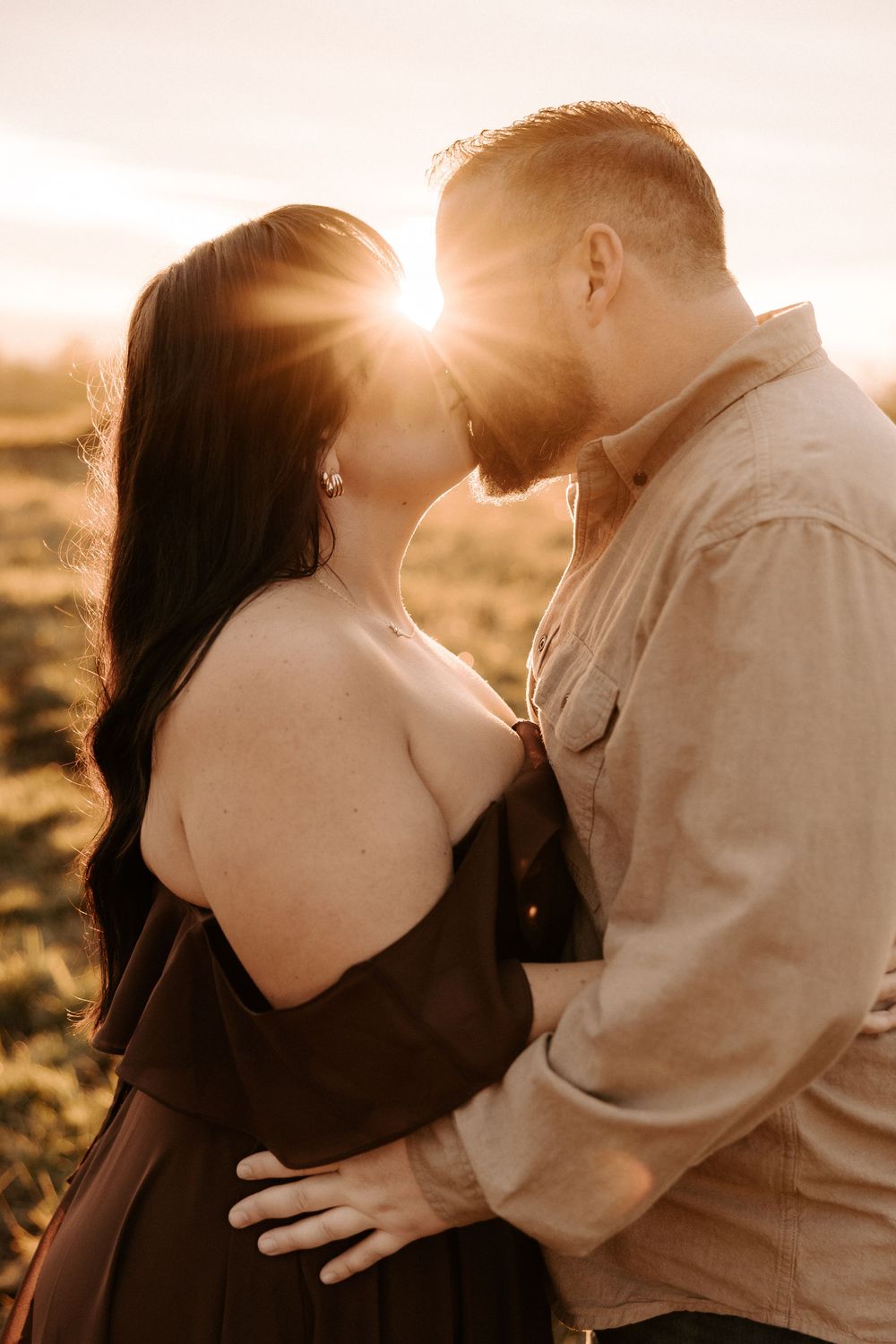 A tender moment between a couple backlit by golden sunlight during an outdoor portrait session.