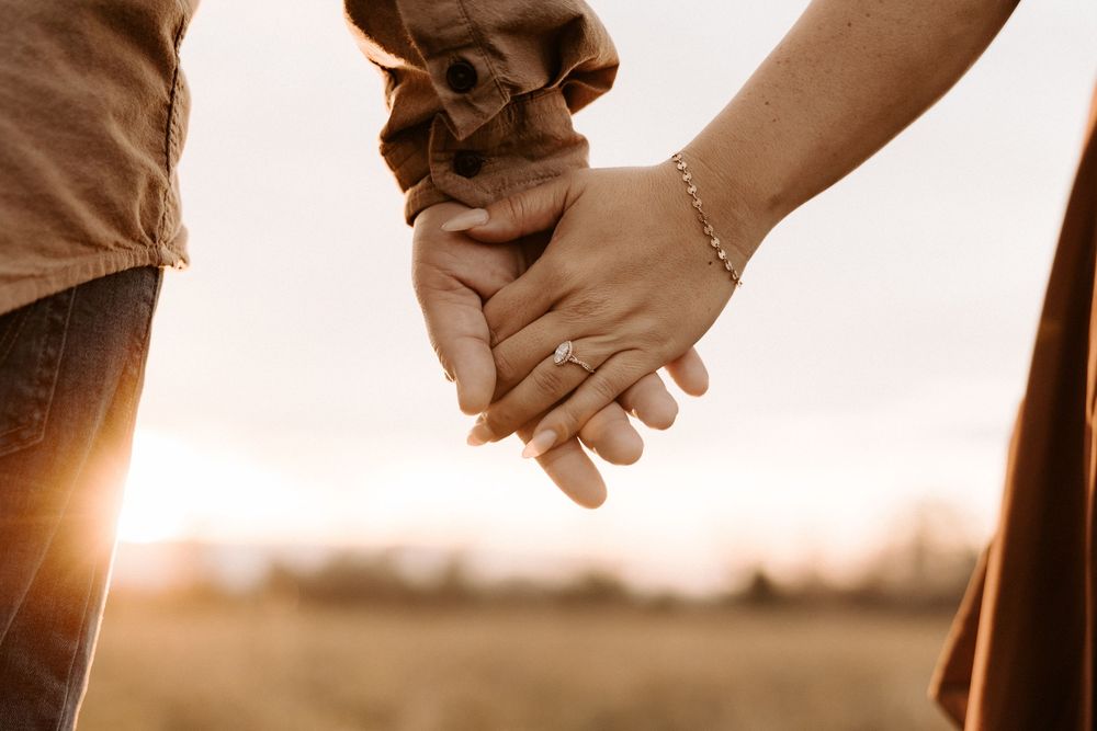 Close-up shot of two hands holding each other tenderly against a soft, warm-toned background.