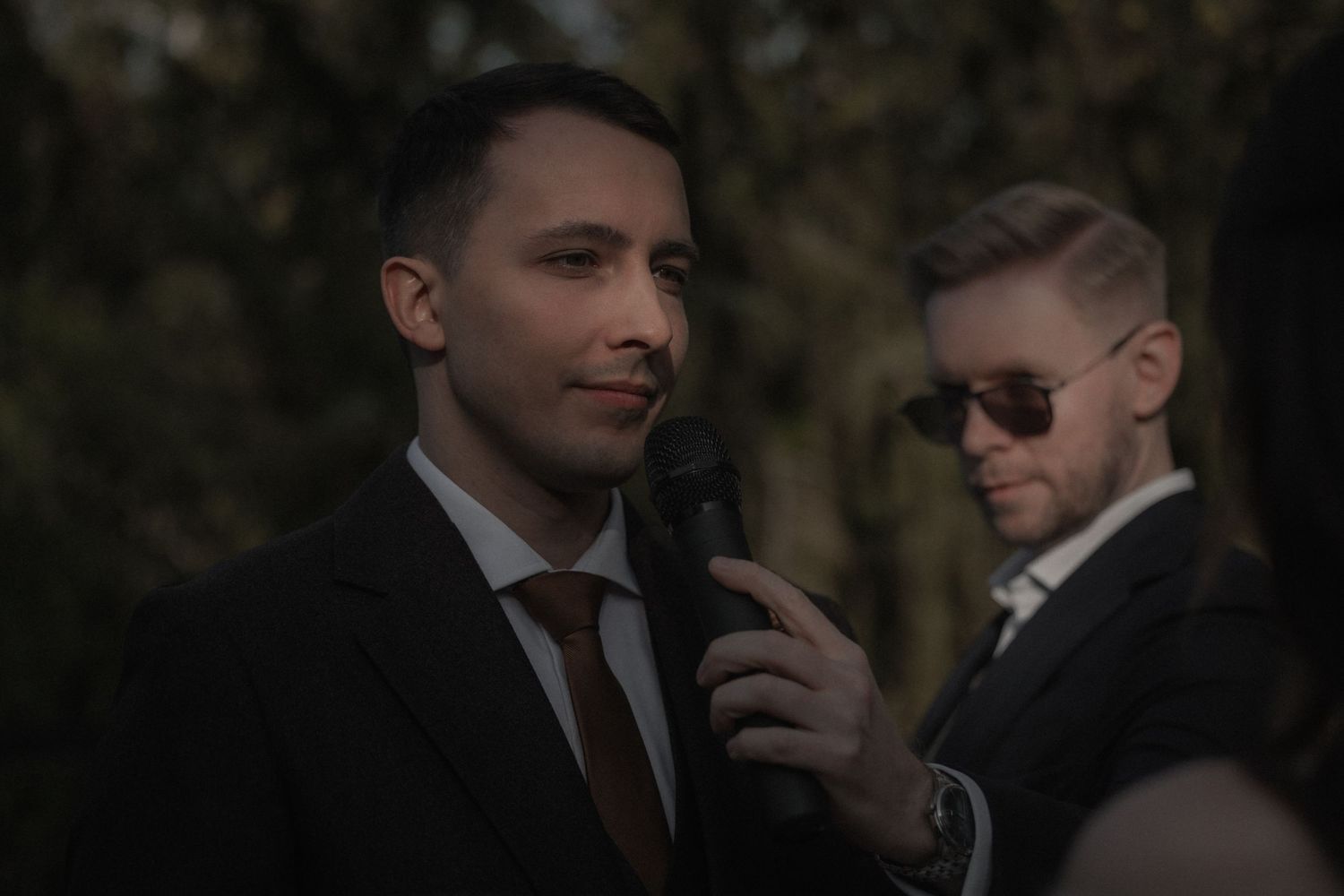 A group of well-dressed men in suits and sunglasses stand together at an outdoor event.