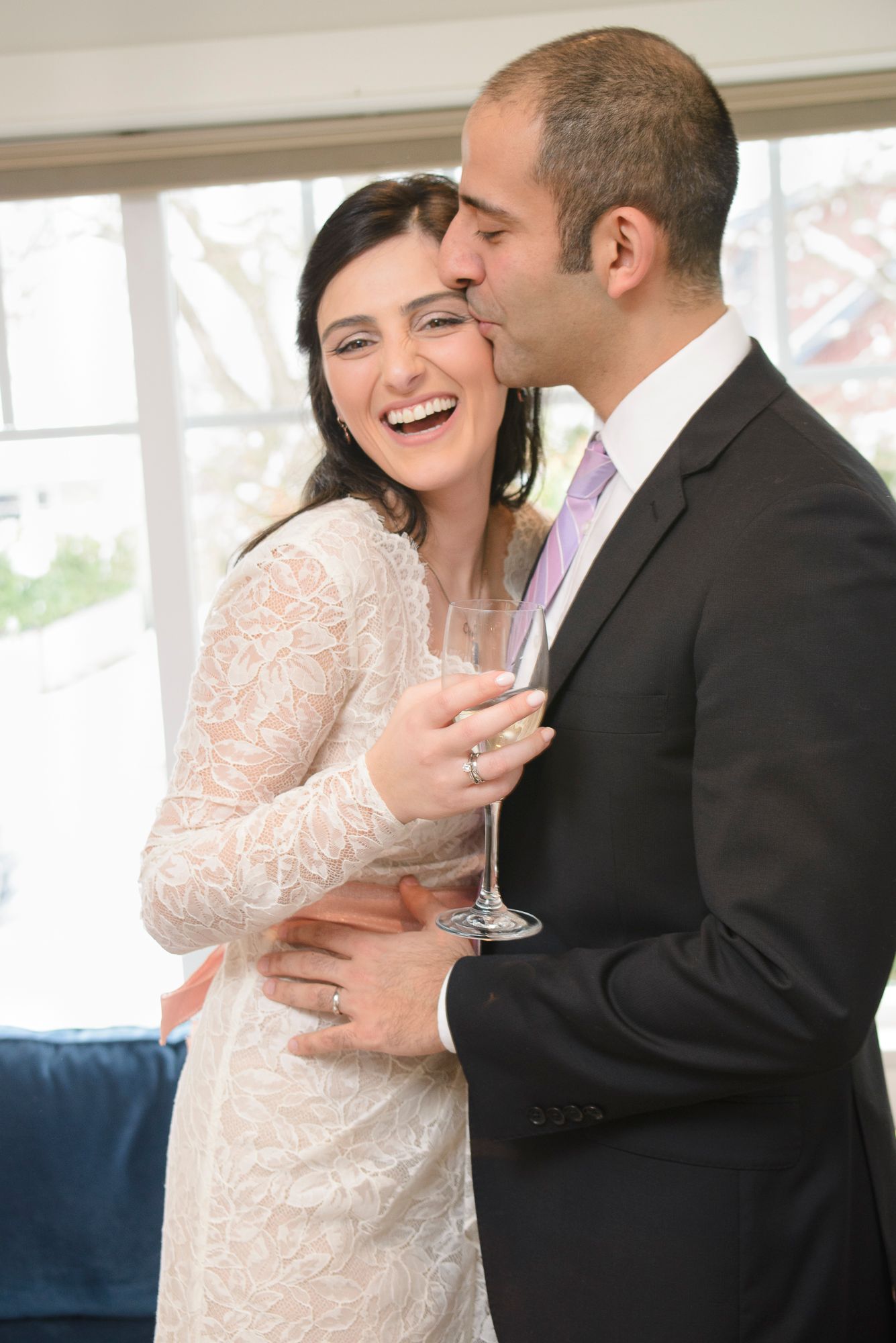 A happy couple shares an intimate moment at their wedding celebration while holding champagne glasses.