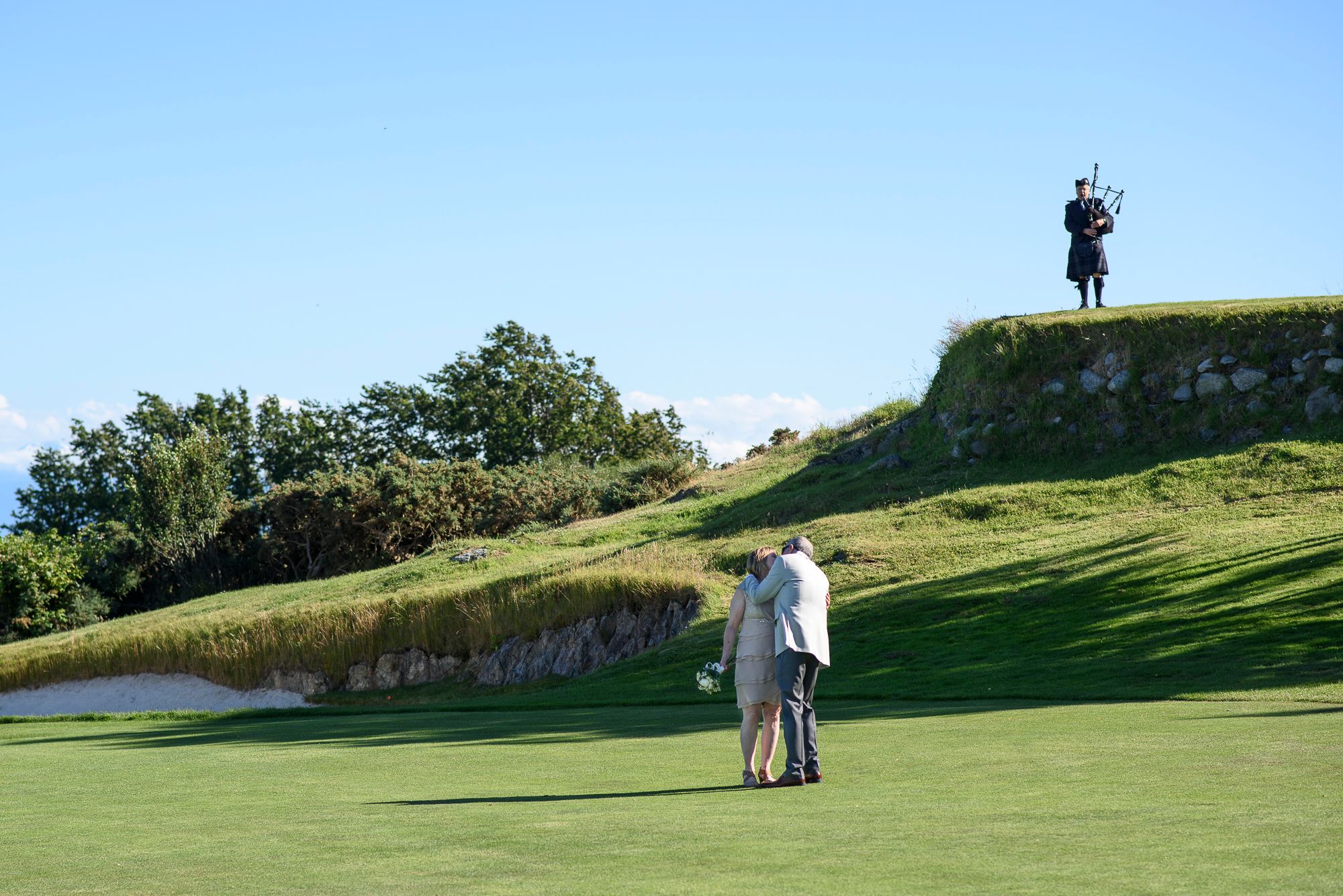 Golfers putting on a scenic coastal golf course with a silhouetted figure standing on a hilltop in the background.